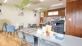 明るい室内の相談スペース。観葉植物とPOPが置かれたテーブル席が複数ある。