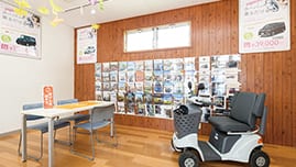 室内の壁面にカタログが並び、相談用のデスクとセニアカー（ハンドル形電動車いす）が展示されている。