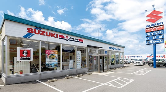吉崎モータース本店の外観。SUZUKIの看板とガラス張りの店舗がある駐車場付きの建物。