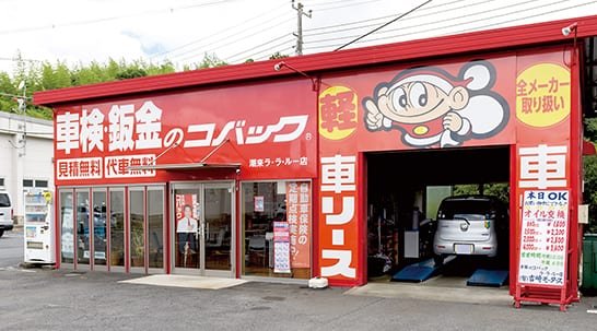 吉崎モータース ラ・ラ・ルー店の外観。赤い看板とキャラクターが描かれた建物で、整備スペースとガラス張りの店舗が並んでいる。